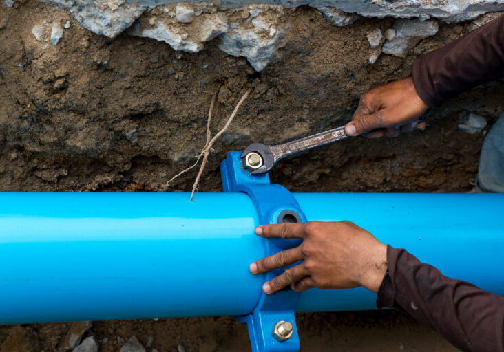 Man using a large wrench on water pipes. Construction site with new Water Pipes in the ground. Sewer pipes to repair or restore in street city.